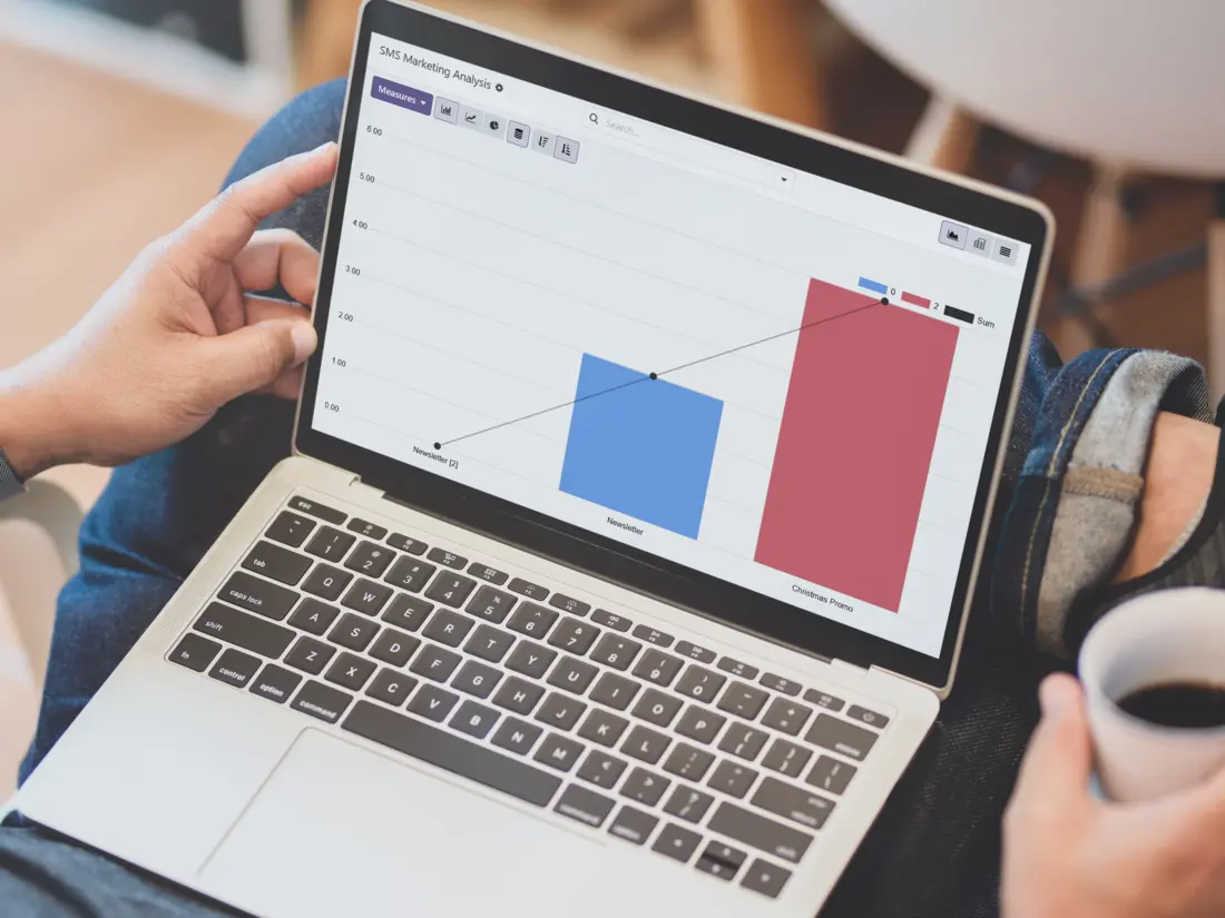 Una persona tomando café y utilizando la aplicación de marketing por SMS en su ordenador