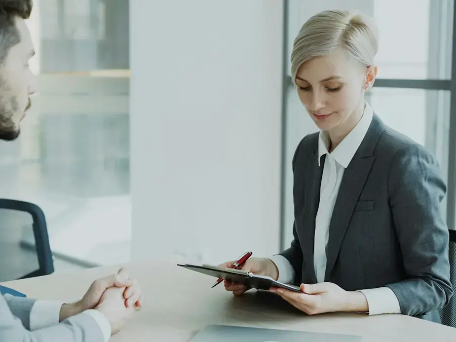 Un hombre y una mujer sentados en una oficina; la mujer sonríe mientras mira un cuaderno