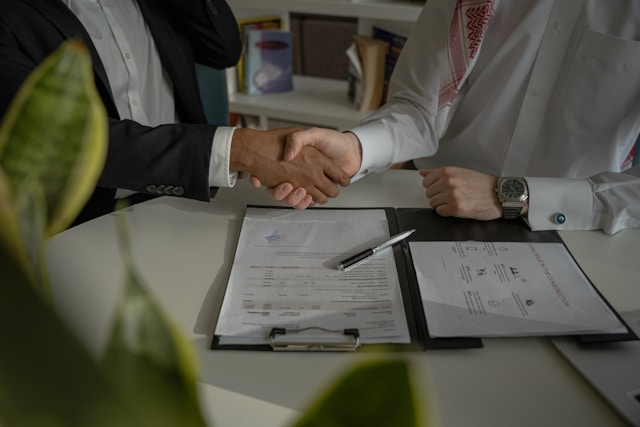 Two people shaking hands next to a signed document on the table